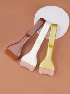 Flat tongue-shaped foundation brushes in brown, white, and gold on a modern platform