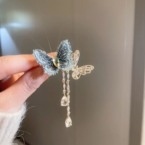 Detail of gold-plated butterfly brooch with blue fabric, crystals and hanging chain tassels