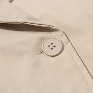 Dettaglio della trama del tessuto twill beige e del bottone coordinato a quattro fori sul cappotto