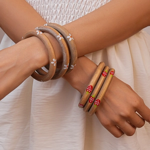 Detailed view of layered wooden bangles with daisy and strawberry prints on a model