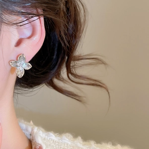 Close-up of minimalist silver flower stud earrings with sparkling cubic zirconia on ear