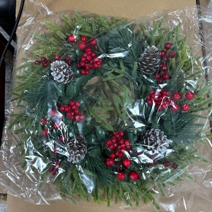 Detail view of a Christmas wreath with green pine branches, red berries and snowy pinecones