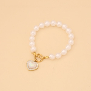 Bracelet perles blanches avec fermoir OT doré et pendentif cœur étincelant sur fond beige