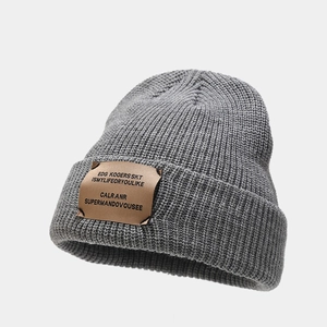 Close-up of grey knitted beanie featuring a textured brown faux leather logo patch
