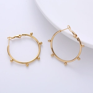Detail of golden hoop earrings featuring delicate bead embellishments on a white backdrop