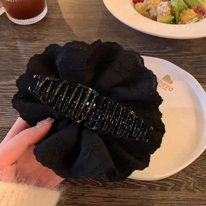 Close-up of a large black lace embroidery bow hair claw clip held by hand in a café