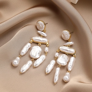 Macro view of long gold tassel earrings featuring irregular baroque pearls on champagne silk