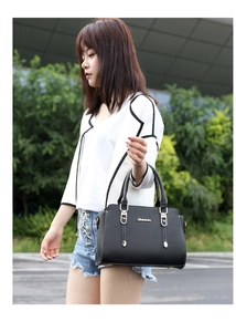 Close-up of elegant black lychee texture handbag with golden hardware on female model