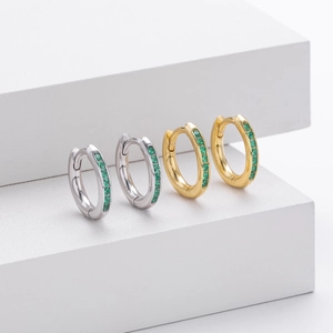 Macro view of silver and gold hoops with emerald green zircons on white display