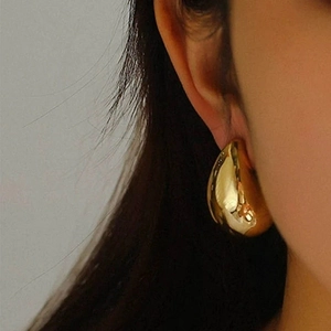 Polished golden hollow teardrop stud earrings for women shown on a model side view