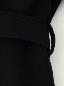 Détail de la boucle de ceinture et de la texture du manteau en laine noir pour femme