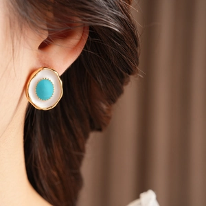 Close-up of vintage gold oval earrings with turquoise and white enamel on a model