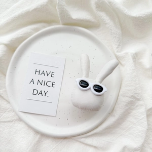 Detail of cute white plush bunny phone grip with sunglasses on a white ceramic plate