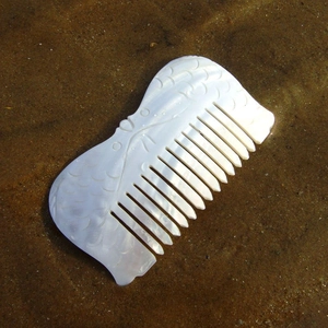Handcrafted fish-shaped seashell hair comb with iridescent luster on a beach