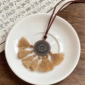 Gros plan détaillé du collier bohème avec pompons kaki et pendentif floral en métal