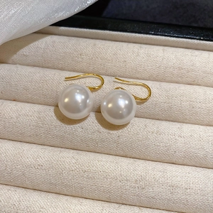Detailed close-up of gold hook earrings with white pearl pendants in a beige jewelry box
