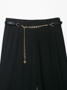 Dettaglio di pantaloni neri con una cintura decorativa a catena in metallo dorato in vita