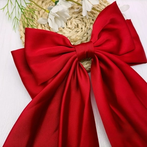 Macro shot of dark red satin bow hair clip with glossy silk texture on white wooden desk