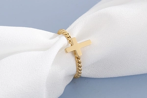 Detailed close-up of golden cross ring with twisted rope band on white silk fabric