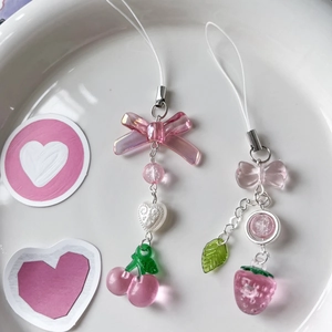 Detailed view of pink cherry and strawberry charms with bows on a ceramic plate