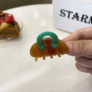 Brown acetate hair claw clip with colorful number pattern held by a hand