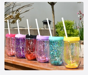 Close-up of colorful glitter insulated tumblers with straws on a wooden deck outdoors