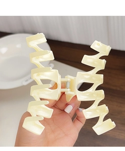 Détail d'une grande pince à cheveux crème montrant la taille et le design ondulé