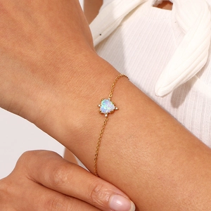 Detailed view of a gold-plated heart-shaped opal pendant bracelet on a woman's wrist
