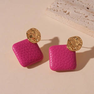 Square fuchsia textured faux leather and hammered gold metal earrings on beige surface