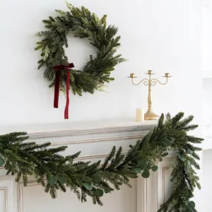 Realistic Christmas PE pine wreath with red velvet bow on a white fireplace mantel