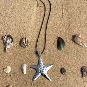 Silver metallic starfish pendant with spiral texture on black cord over beach sand