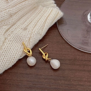 Detailed view of knot-design gold pearl earrings on a dark wood surface