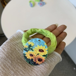 Detail of green fabric hair tie featuring an oval sunflower pendant in a French style