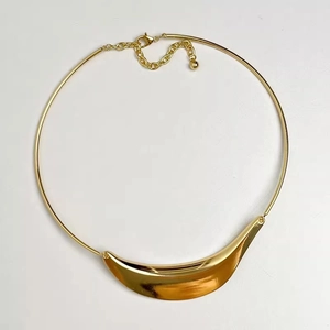 Detail view of a polished gold crescent pendant on a minimalist stiff collar necklace