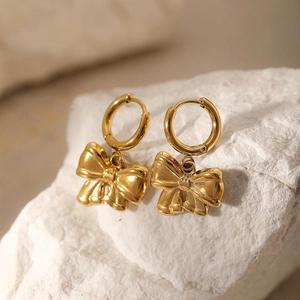 Gold stainless steel hoop earrings with elegant bow pendant on a white stone background
