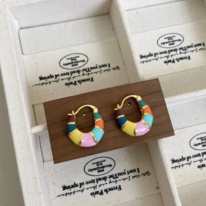 Détail des boucles d'oreilles en émail arc-en-ciel sur un support en bois chic