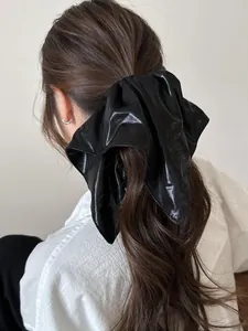 Close-up of a large black glossy leather scrunchie bow tied on a high ponytail