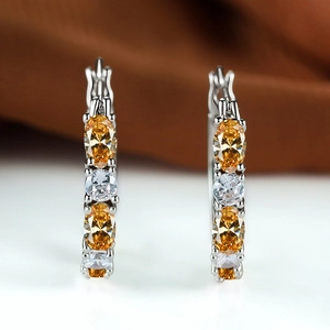 Macro detail of silver hoop earrings with oval orange stones and white round zircons