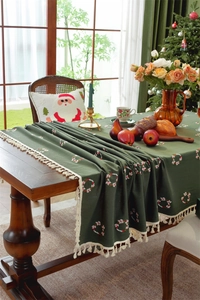 Detailed close-up of dark green Christmas table runner with embroidered wreaths and tassels