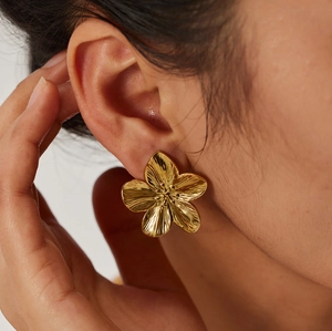 Macro detail of textured gold flower stud earring worn by a model in a side profile view