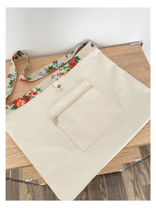 Detail of off-white canvas tote with floral strap, metal zipper pocket and button decoration