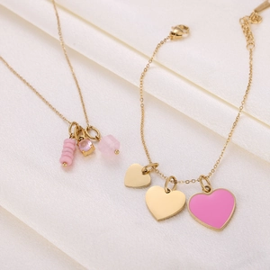 Detail of gold necklace and bracelet set with pink heart charms on white silk background