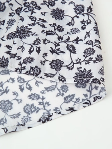 Détail de l'ourlet incurvé et des coutures précises sur une chemise à fleurs blanches
