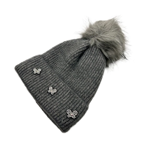 Detail of gray knit beanie with large pom-pom and sparkling rhinestone butterfly accents