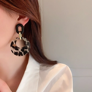 Close-up of leopard print acrylic hoop earrings worn by a model in soft natural lighting