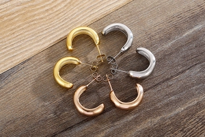 Polished C-shaped hoop earrings in gold, silver, and rose gold on dark wood background