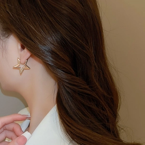 Close-up of elegant gold star-shaped hollow hoop earring worn on a model's ear