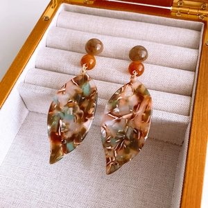 Detailed close-up of leaf-shaped tortoiseshell acrylic earrings in a wooden jewelry box
