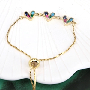 Macro detail of adjustable gold bracelet featuring three heart-shaped multi-color zircon charms