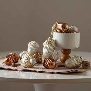 Champagne and bronze acorn Christmas tree ornaments set on a snowy decorative surface